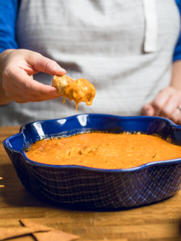A hand holding a chip with vegan buffalo chicken dip.