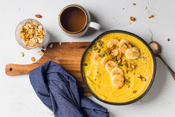 A vegan mango smoothie bowl on a wooden board with a cup of coffee.