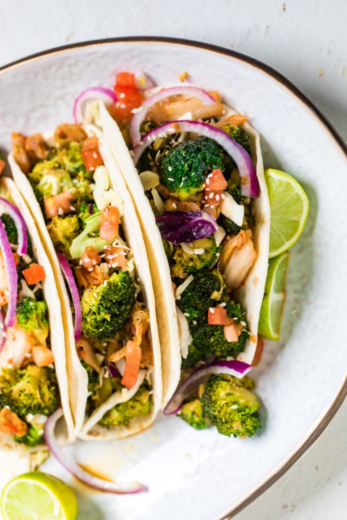 Three Korean inspired vegan broccoli tacos with lime wedges.