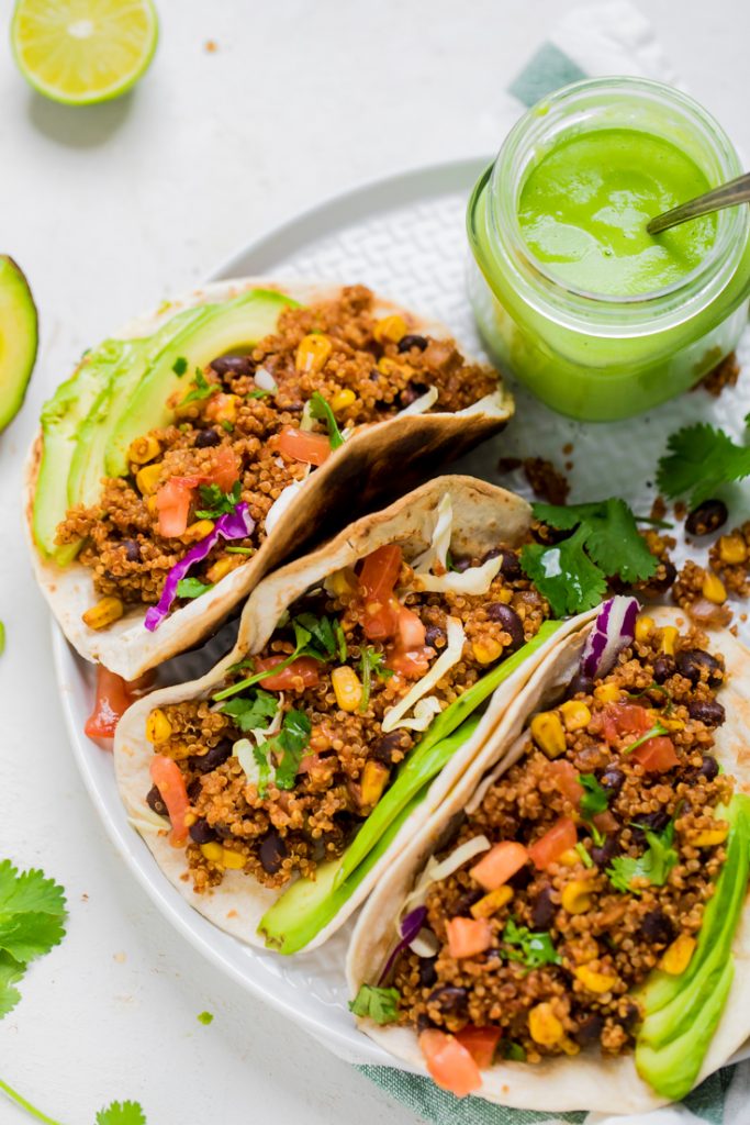 A plate of vegan quinoa and black bean tacos with a jar of avocado sauce.