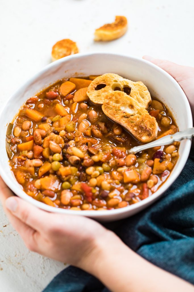Hands holding a bowl of instant pot vegan bean soup.