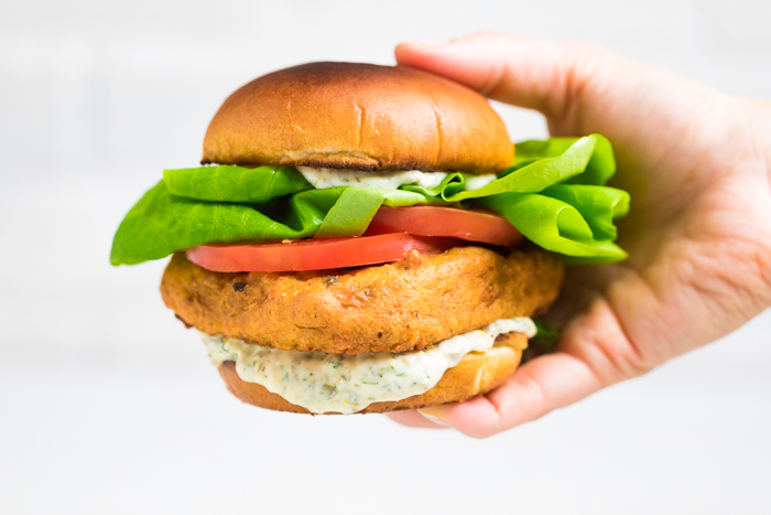 A hand holding a vegan fish sandwich with vegan tartar sauce.