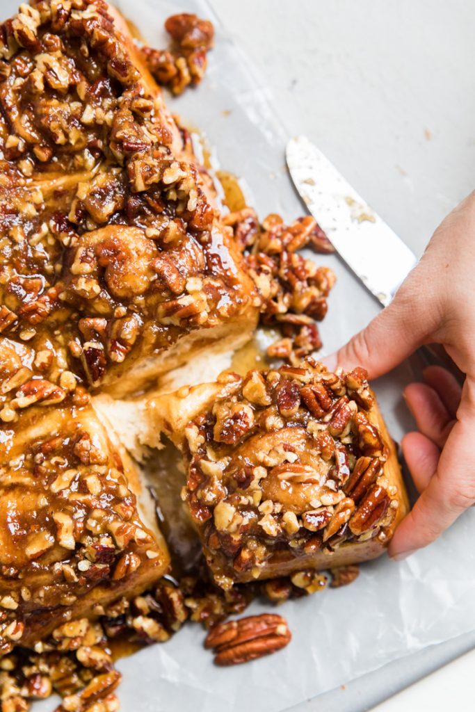 A hand pulling off a vegan sticky bun from the batch.