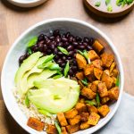 A cajun sweet potatoes and black beans rice bowl with avocado slices.