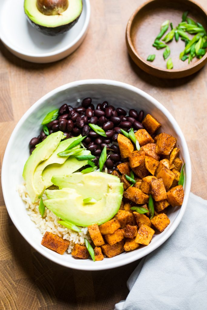 A bowl of rice with avocado slices, sweet potatoes and black beans. 