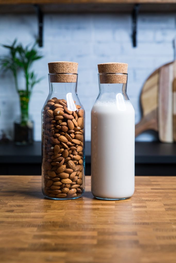 A glass of almonds next to a glass of homemade almond milk. 