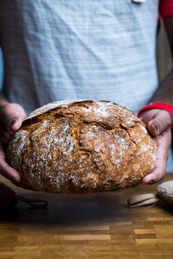 A person holding a loaf of vegan artisan bread.