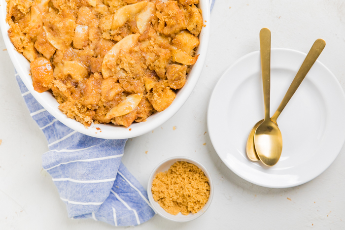 Vegan apple pie French toast casserole in a dish next to a white plate with gold spoons.