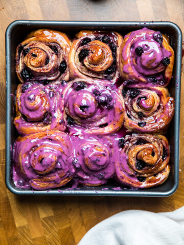 A tray of vegan blueberry cinnamon rolls cooked and topping with blueberry glaze.