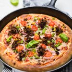 vegan walnut meat skillet pizza topped with tomatoes and basil.