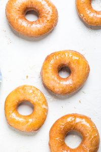 Fried vegan glazed donuts on a white table.