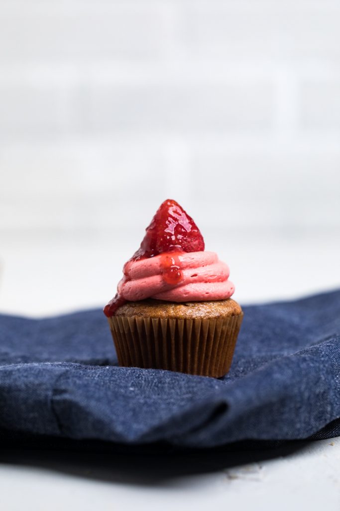 A dye free vegan strawberry cupcake topped with a strawberry and frosting.
