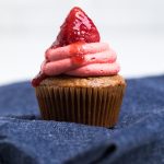 A dye free vegan strawberry cupcake topped with swirled strawberry frosting and a fresh strawberry.