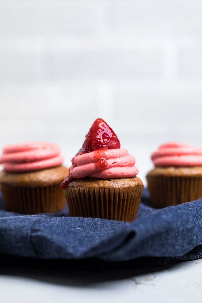 Three vegan strawberry cupcakes topped with frosting. 