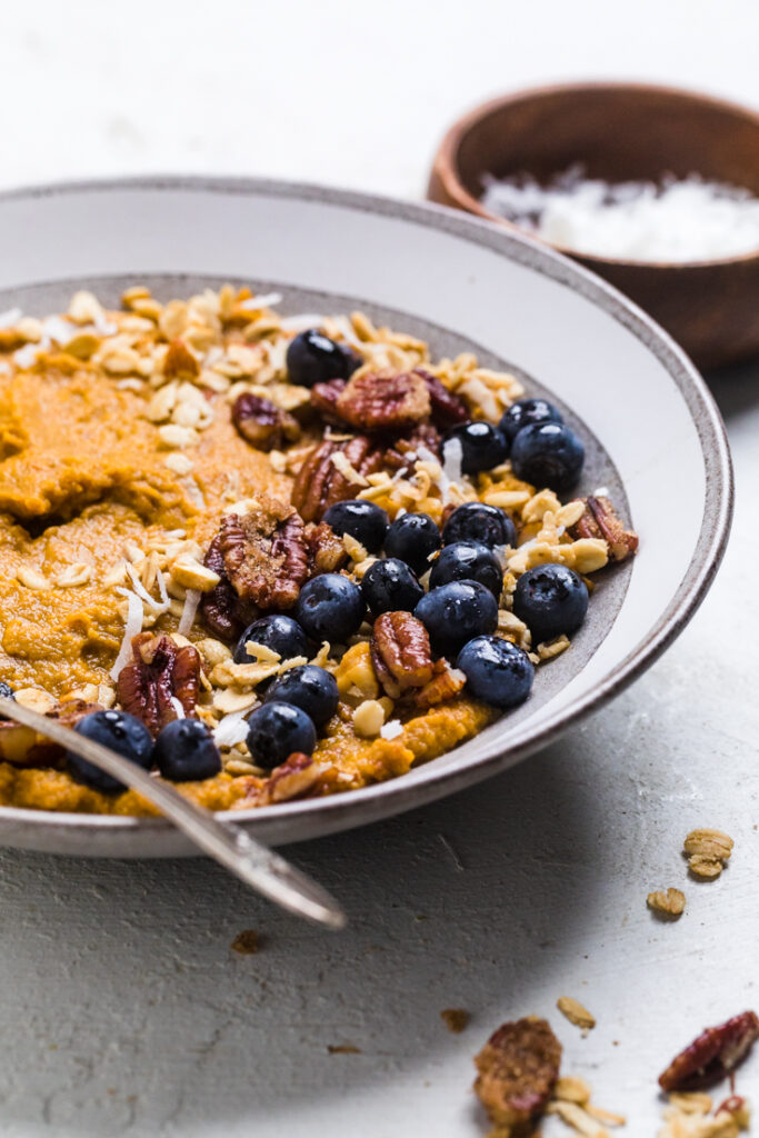 Easy breakfast vegan sweet potato bowl topped with coconut, pecans, and fresh blueberries.