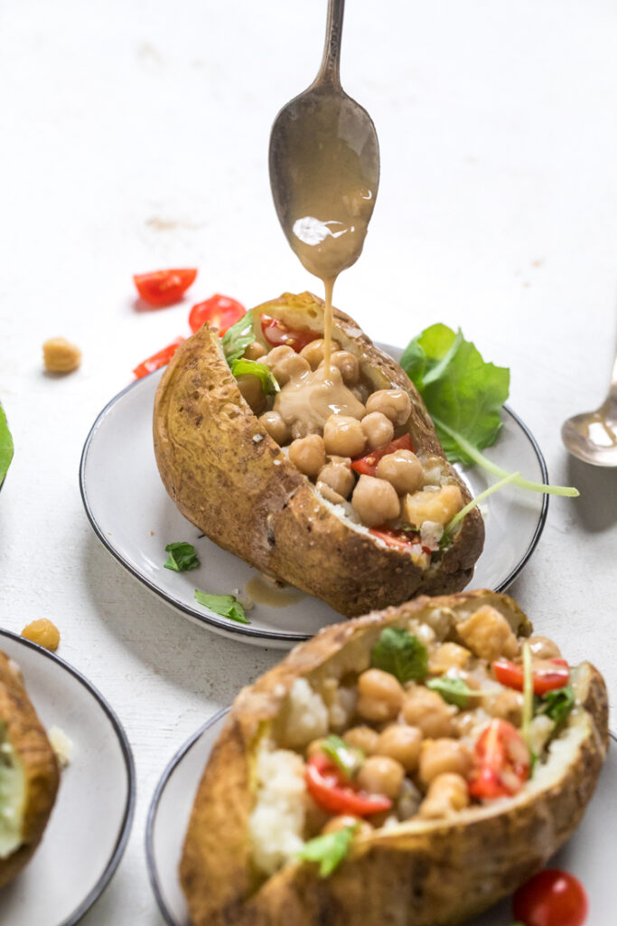 A spoon drizzling sauce over a plate of Chickpea vegan stuffed baked potato.