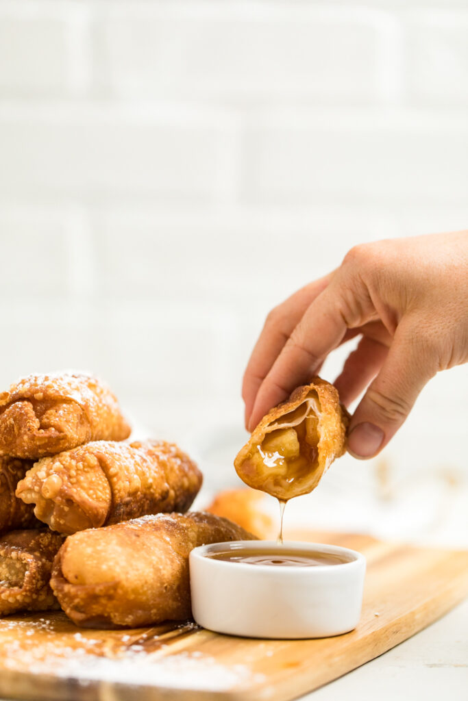 Hand dipping a 2 ingredient vegan apple pie egg roll into vegan caramel sauce with bite out.