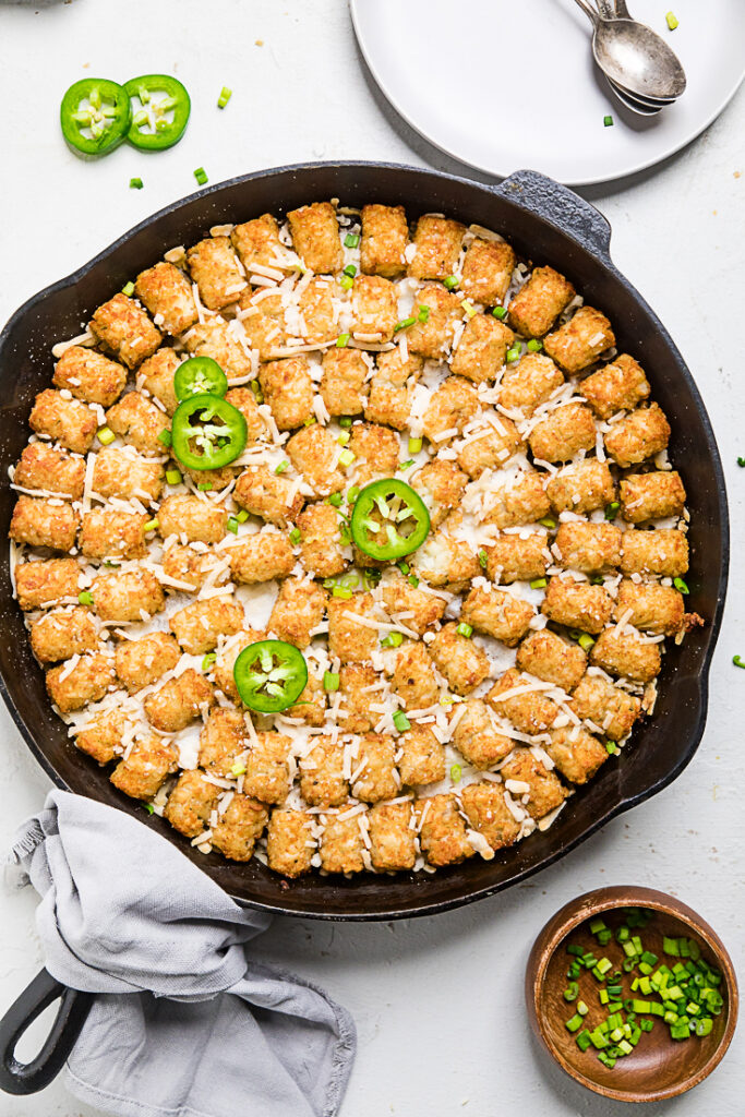tex mex vegan tater tot casserole in a skillet with sliced jalapenos on top 