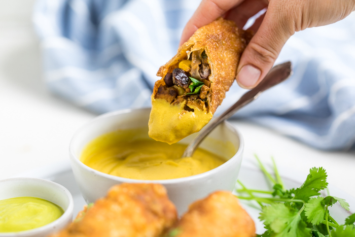 A hand dipping a vegan southwest egg roll in sauce.