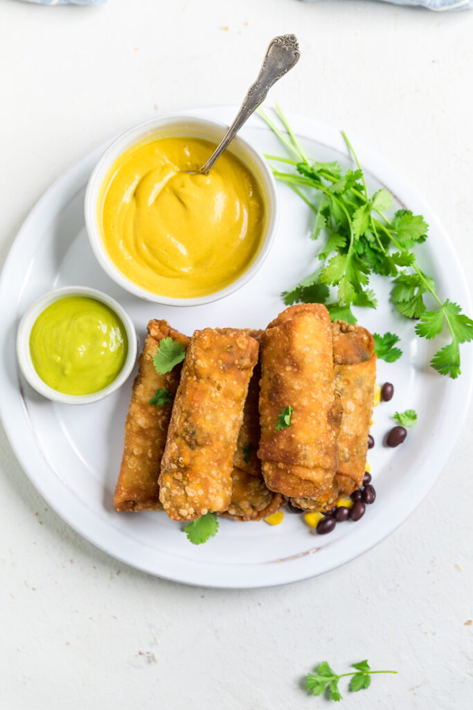 A plate of vegan southwest egg rolls and vegan nacho cheese sauce.