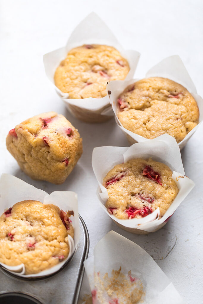 Five vegan strawberry muffins on a white table.