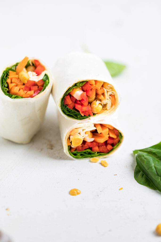 A chickpea veggie wrap with carrots peppers tomatoes and spinach.