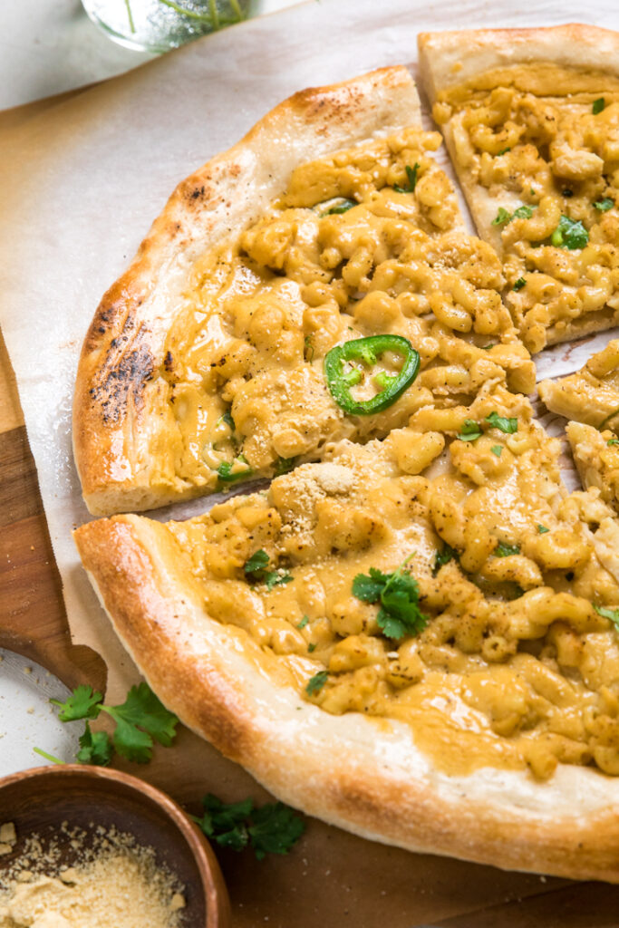 A spicy vegan mac and cheese pizza sliced topped with fresh jalapenos.