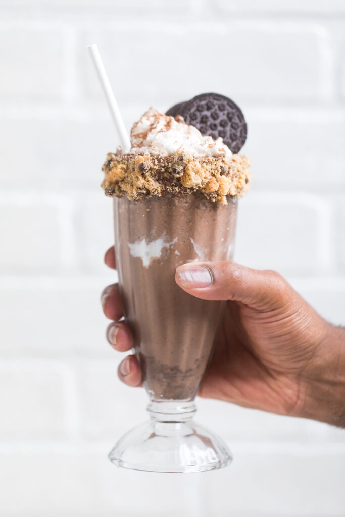 A hand holding a glass of vegan chocolate cookies and cream milkshake.