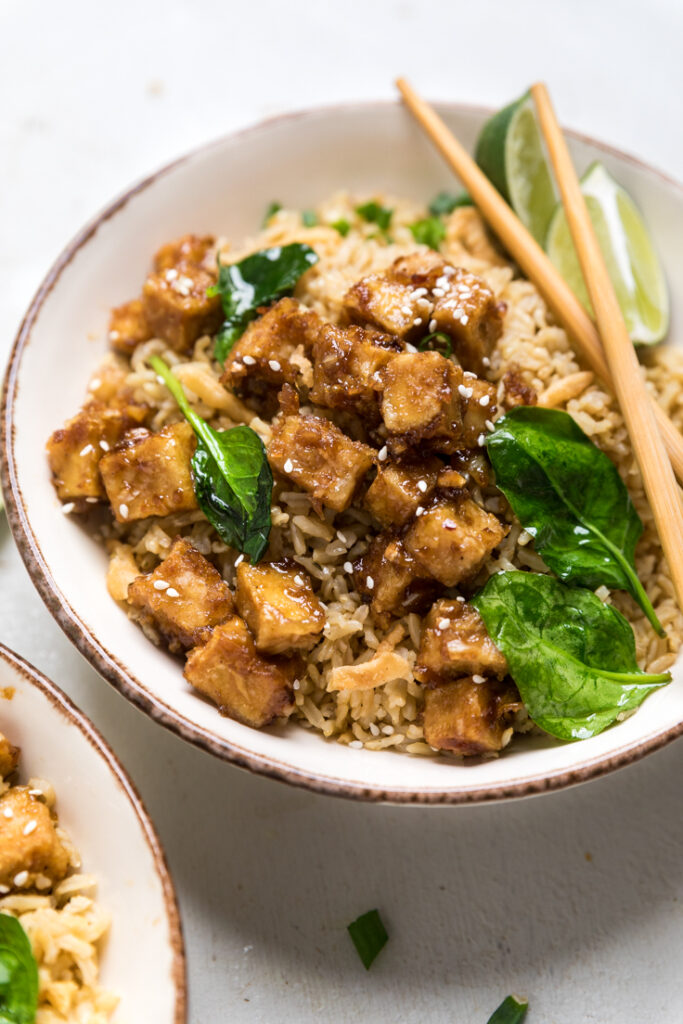 A bowl of saucy Vegan Crispy Tofu in Garlic Sauce with spinach and limes.
