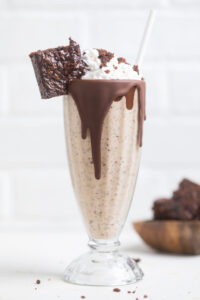 A vegan peanut butter fudge brownie milkshake with chocolate drizzle topped with whip.