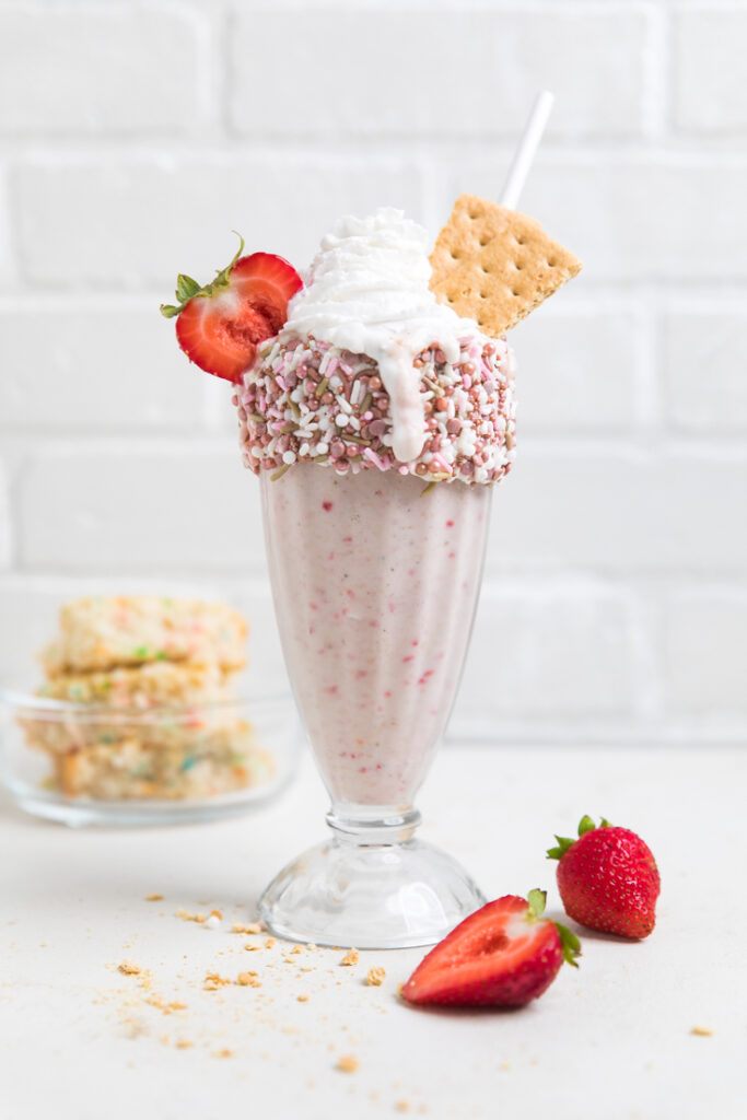 A glass of vegan strawberry birthday cake milkshake rimmed with sprinkles.