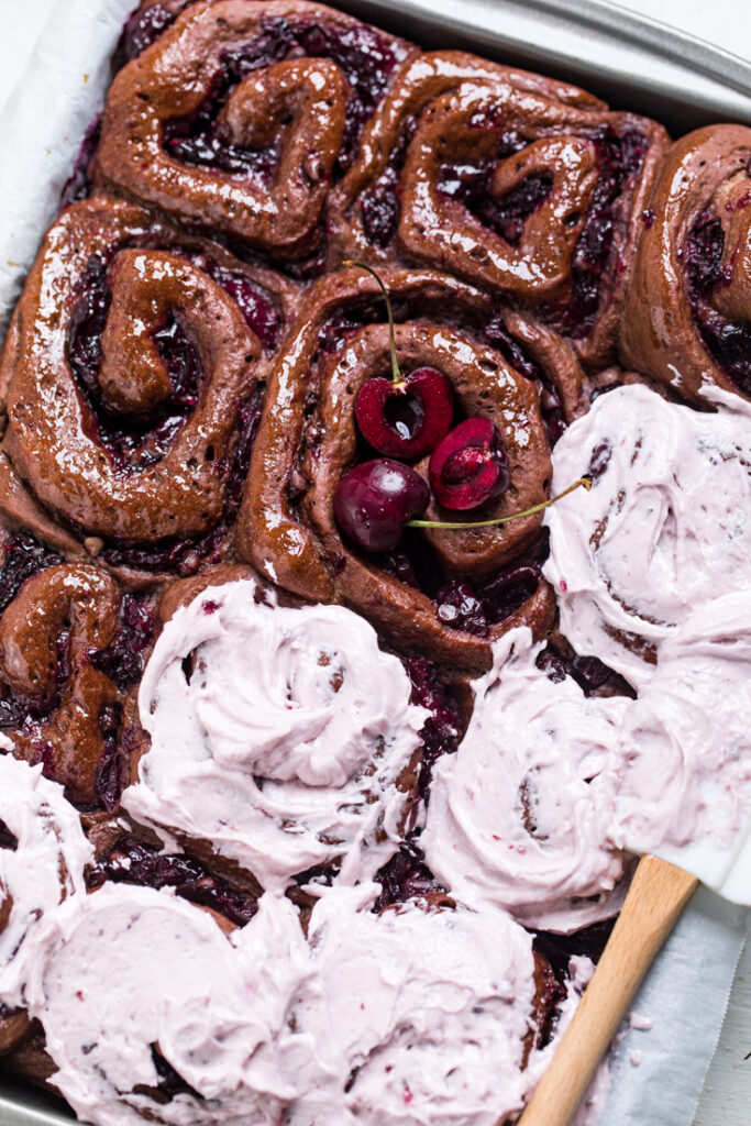 A tray of Dark Chocolate Cherry Vegan Cinnamon Rolls some with frosting.