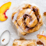 A peaches and cream vegan cinnamon roll on white parchment paper with drizzle.