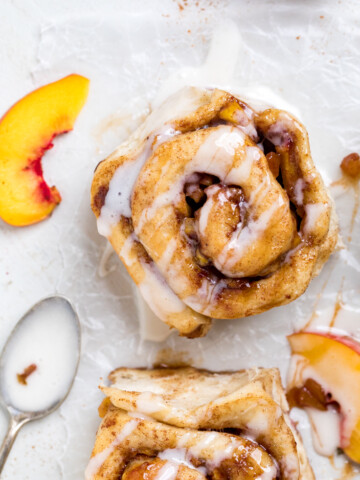 A peaches and cream vegan cinnamon roll on white parchment paper with drizzle.