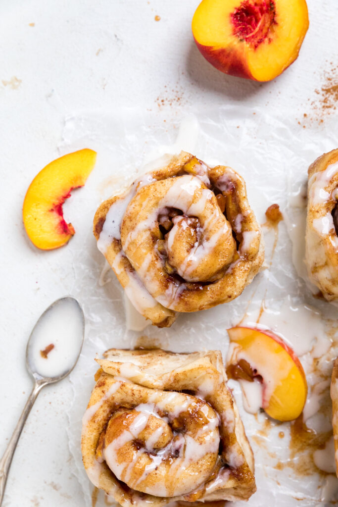Top of cooked Peaches and cream vegan cinnamon roll with fresh peach slices.