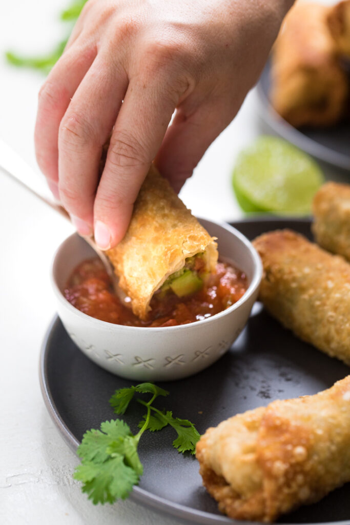 A vegan avocado egg roll being dipped in salsa.