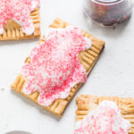 Three Vegan cherry pop tarts with white glaze and pink sprinkles.