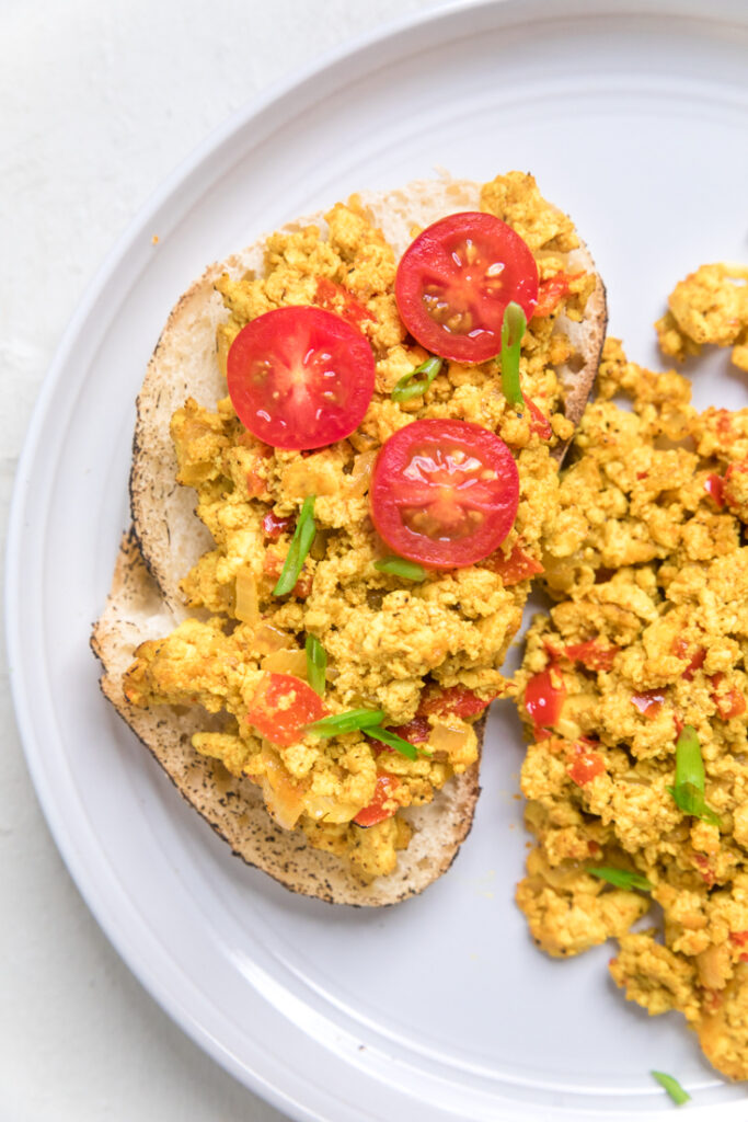 A slice of thick toast with Easy vegan tofu scramble and tomatoes.