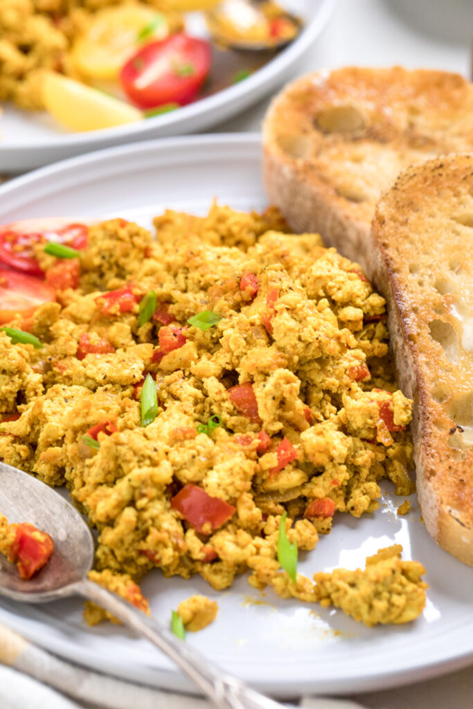 Easy vegan tofu scramble with peppers and onions on a plate with toasty bread. 