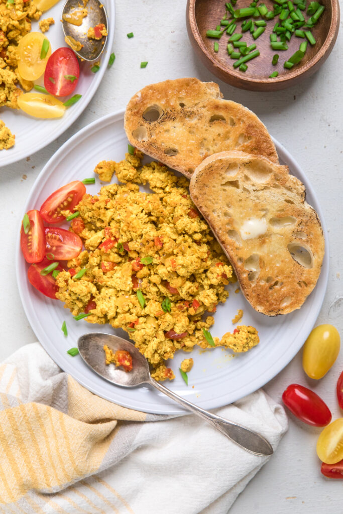 A white plate of Easy vegan tofu scramble with buttered crunchy bread and tomatoes.