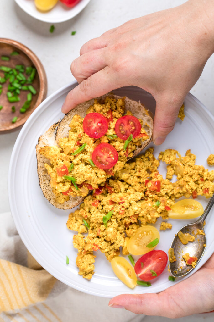 A hand holding Easy vegan tofu scramble on a piece of thick toast. 