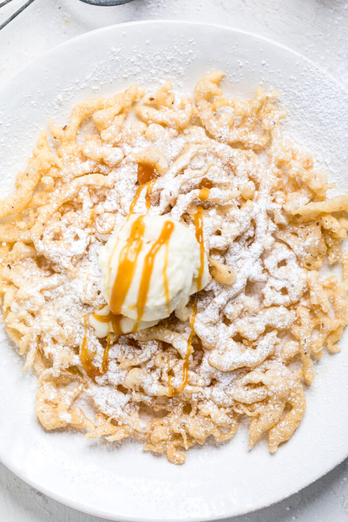 A plate of vegan funnel cake with caramel drizzle and ice cream.