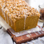 A loaf of gluten free vegan pumpkin bread with glaze drizzled and crumble topping.