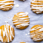 A batch of vegan pumpkin cookies with white drizzled glaze over top.