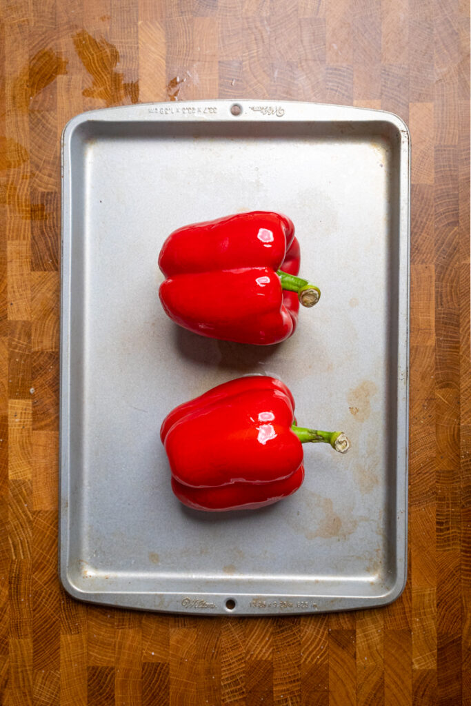 Two Raw Red Peppers on a tray brushed with oil.
