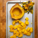 Cubed and a whole half of acorn squash cooked on a tray.