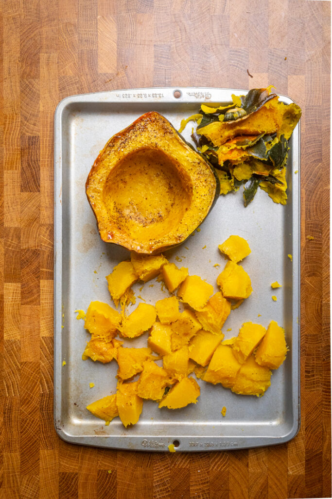 Cubed and a whole half of acorn squash cooked on a tray.