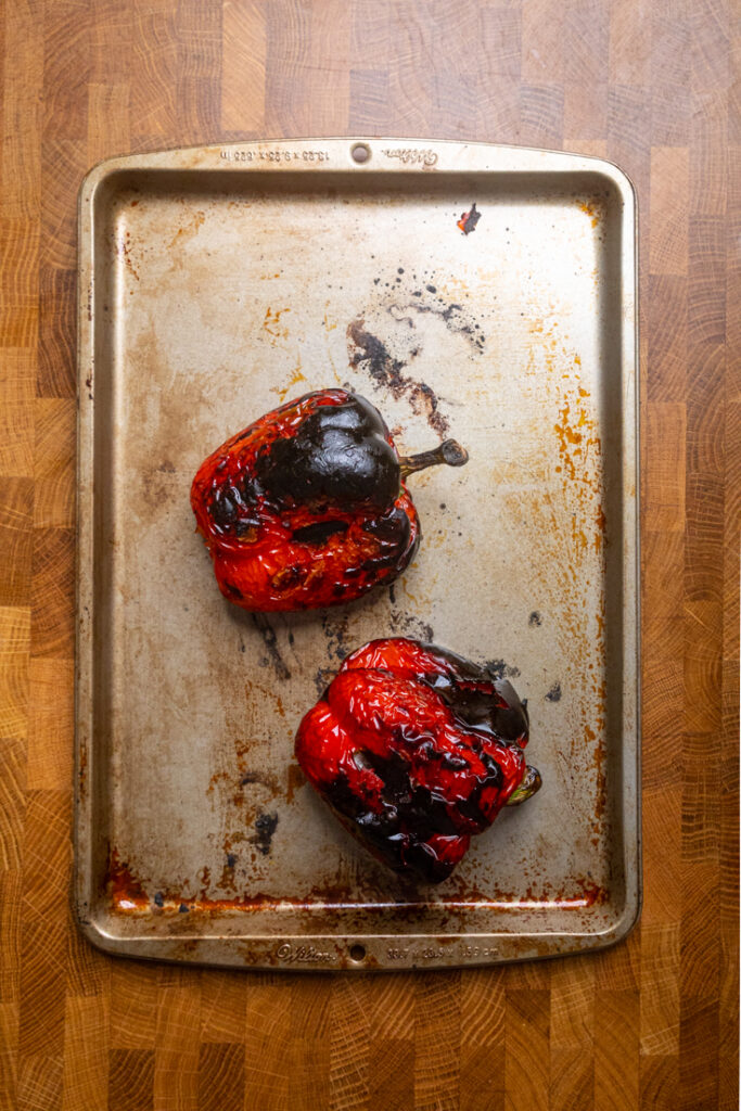 Two charred whole Roasted Red Peppers on a tray.