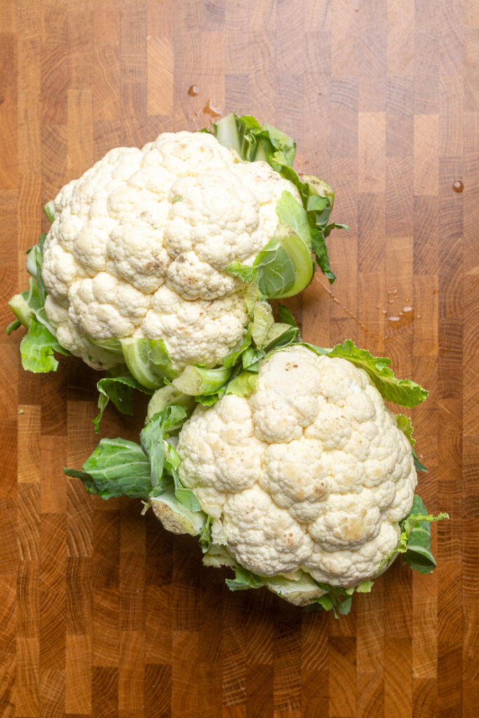 Two heads of cauliflower on a table.