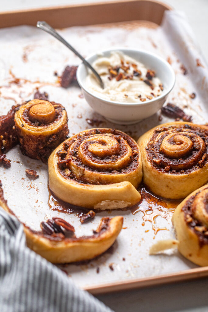 Vegan brown butter pecan cinnamon rolls with a bowl of frosting.